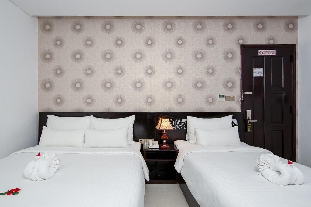 Une chambre d’hôtel avec deux lits, une tête de lit à motifs capitonnés, une table de chevet avec une lampe et une porte sur laquelle est apposé un panneau « Interdiction de fumer ».