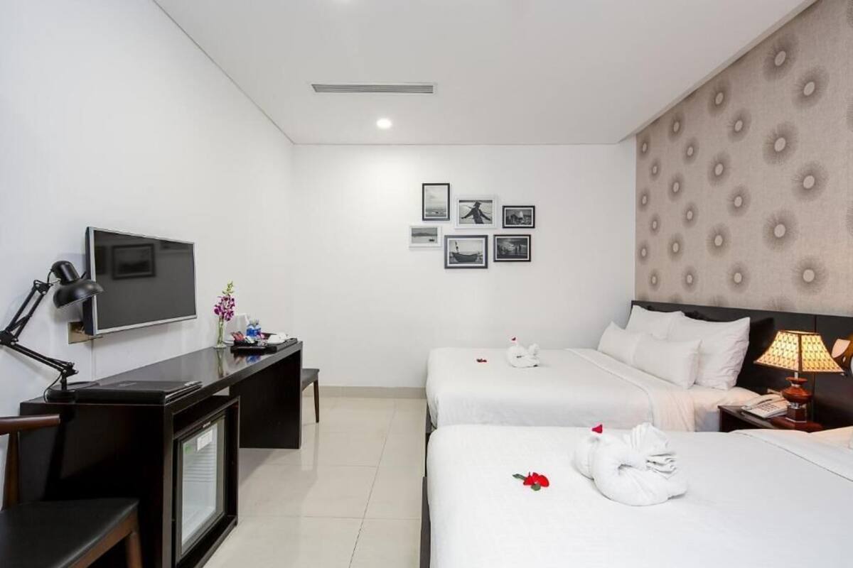 A hotel room with two beds, a desk with a TV, and framed pictures on the wall.