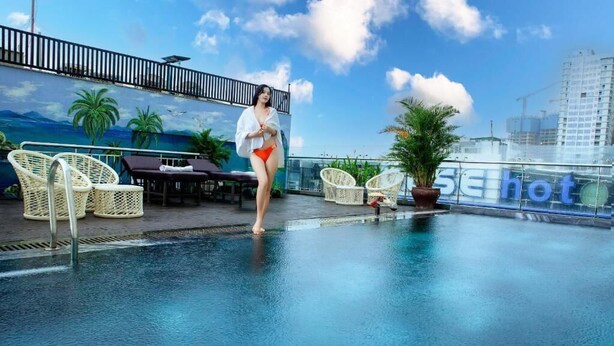 A rooftop pool area with lounge chairs, a mural of palm trees and mountains, and a sign that reads "SE hot". - Dung Nam Hotel (Da Nang)