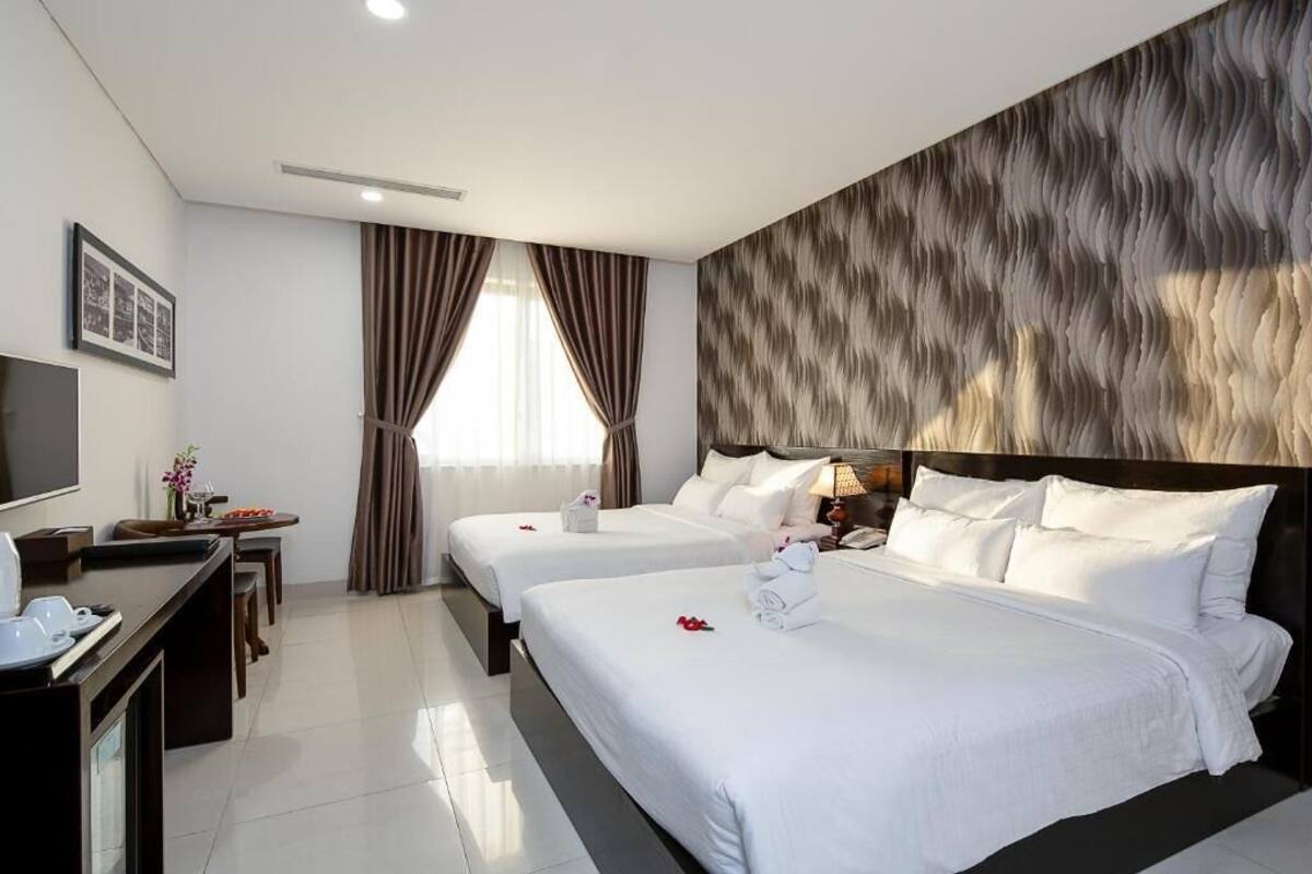 A hotel room with two beds, a TV, a desk, and a window with curtains.