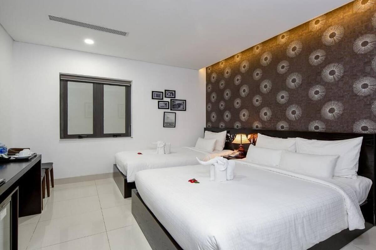 A hotel room with two beds, a desk, a chair, and a window.
