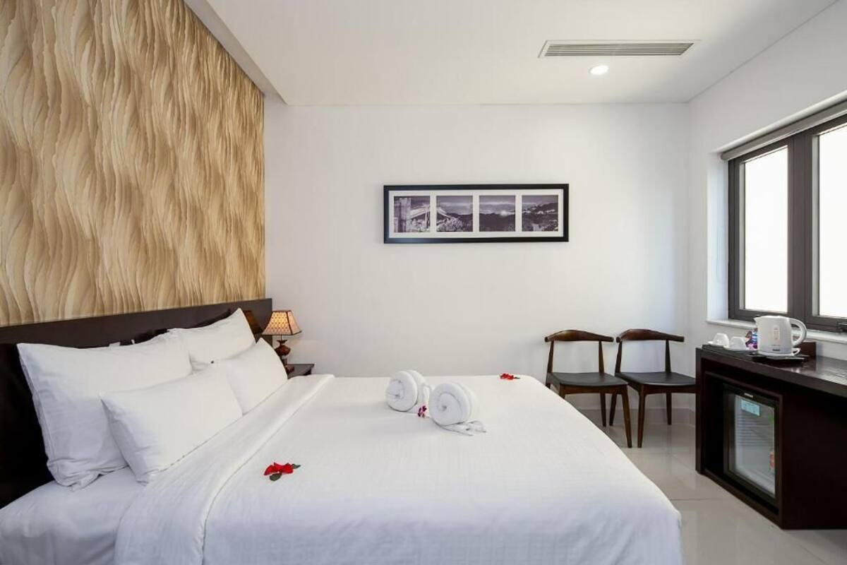 A hotel room with a large bed, a desk with a coffee maker, a chair, and a framed picture on the wall.