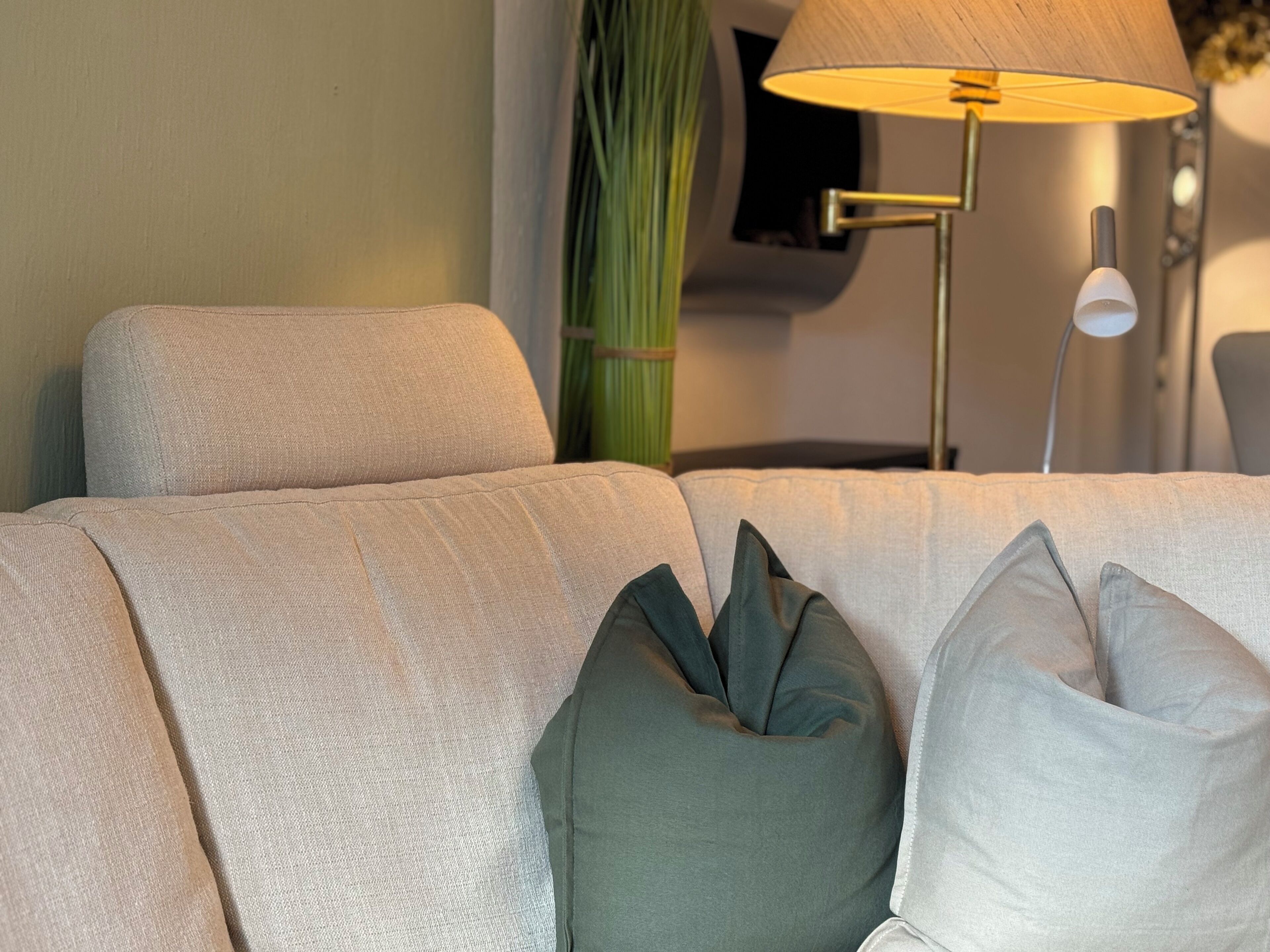 Een bank met een gestructureerde stof, een groen decoratief kussen en een lamp met een witte lampenkap.