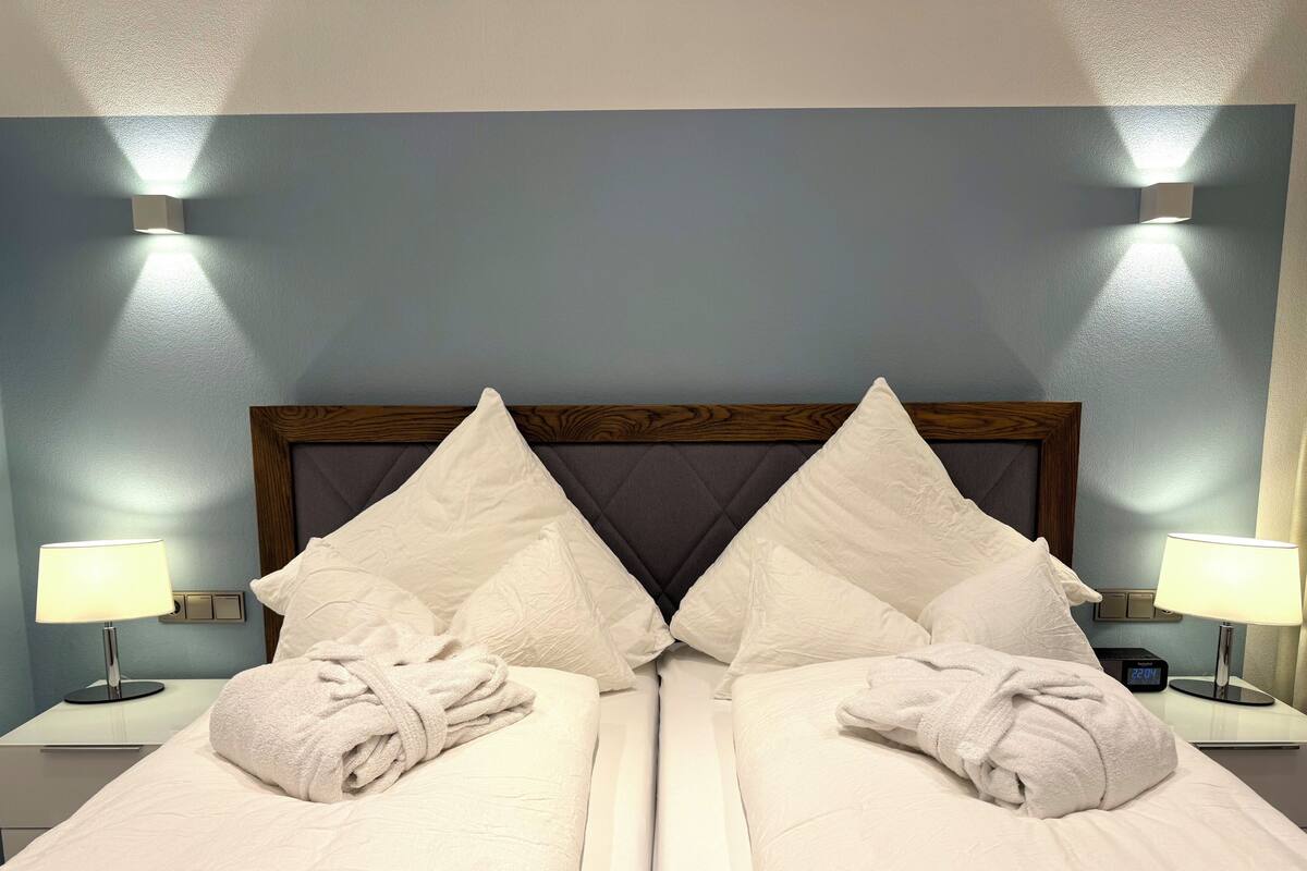 A double bed with a wooden headboard, two bedside tables with lamps, and two towels on the bed.