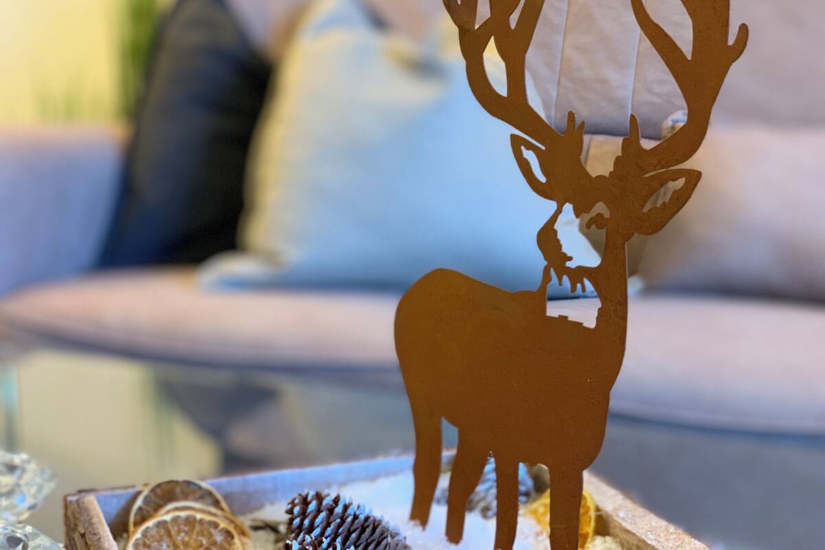 A decorative deer silhouette on a glass table with a blurred background of a couch and cushions.