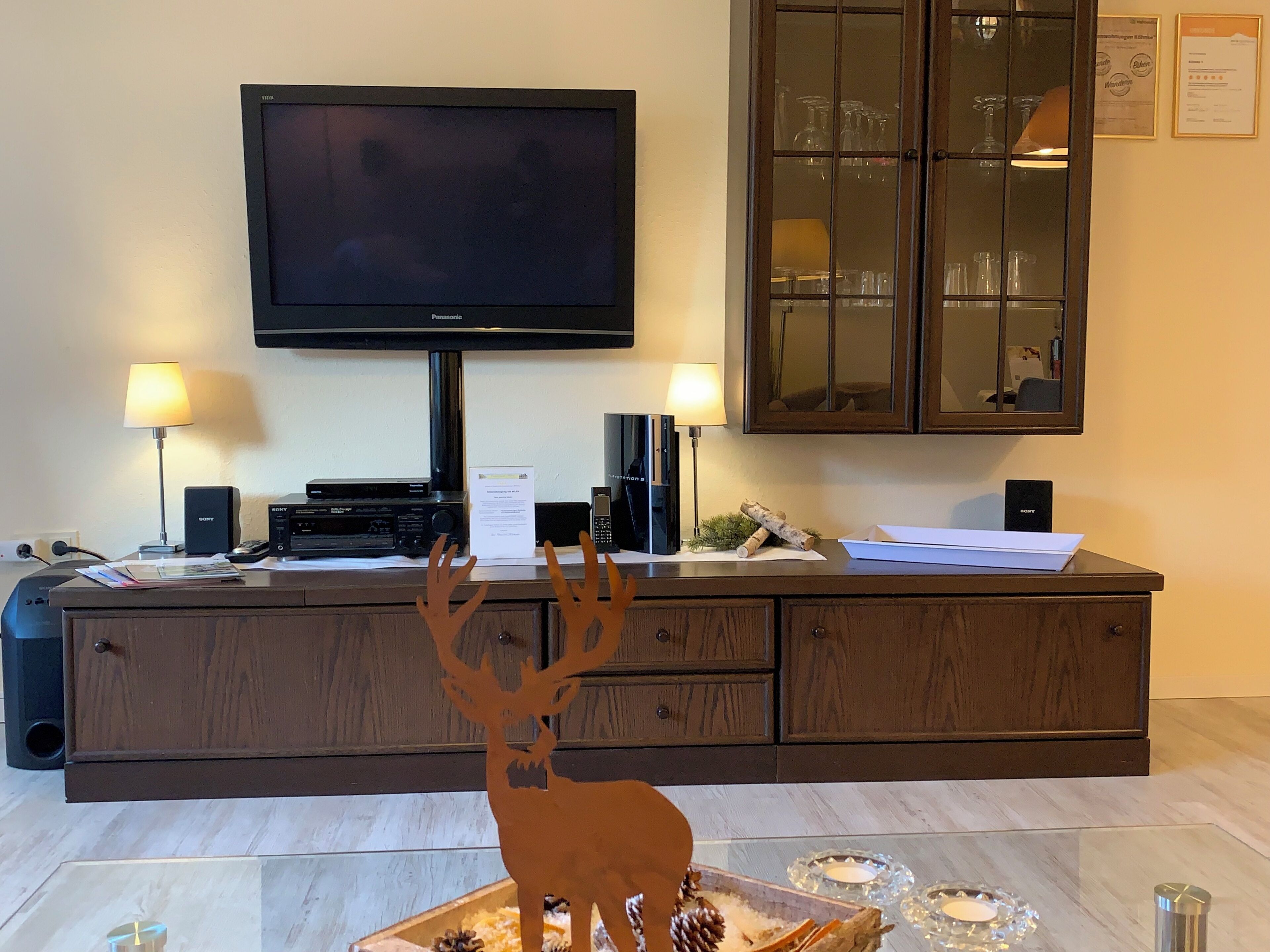 A living room with a flat-screen TV, two lamps, a wooden cabinet, and a decorative deer figurine.
