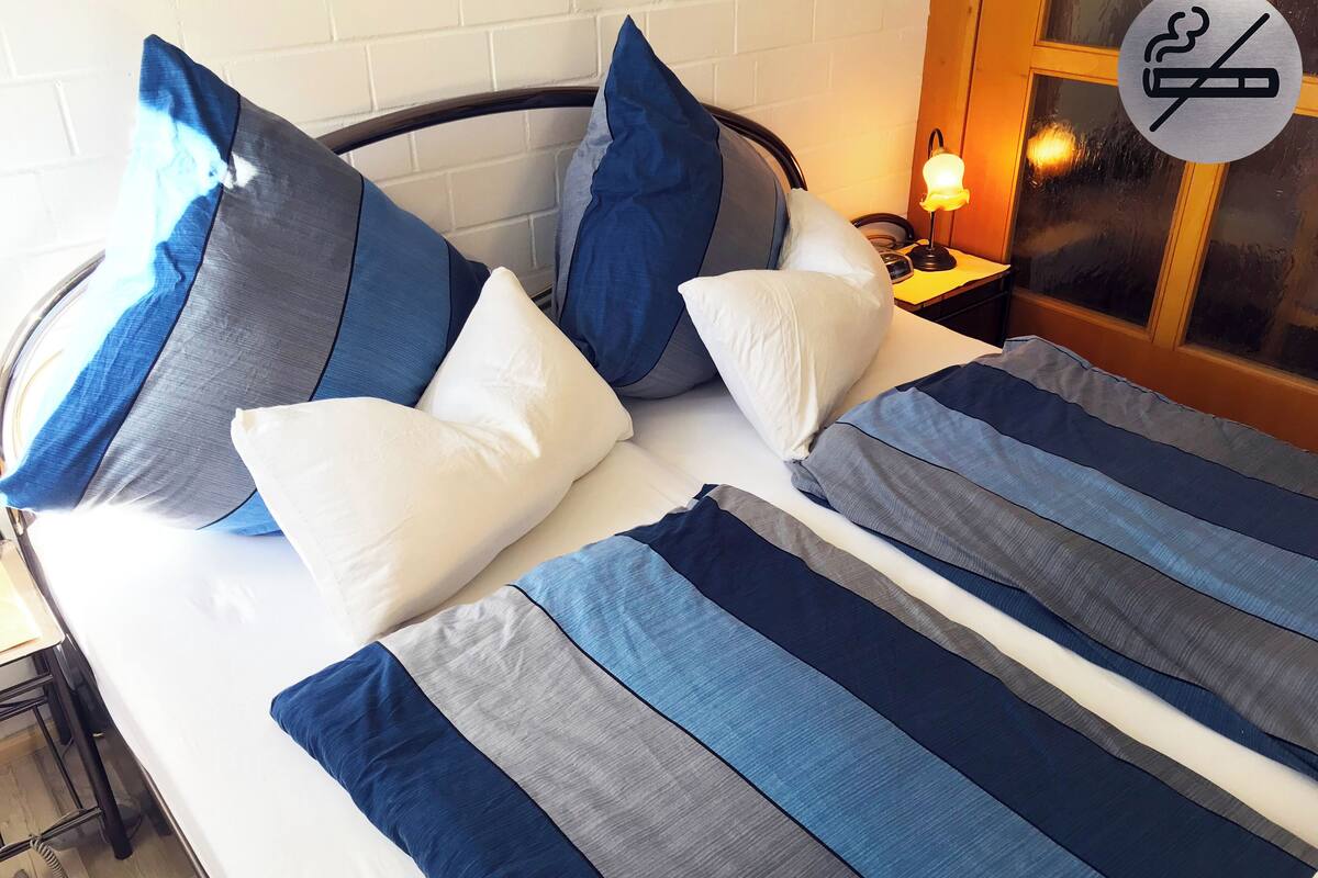 A bed with blue and white striped bedding, a wooden headboard, and a nightstand with a lamp.