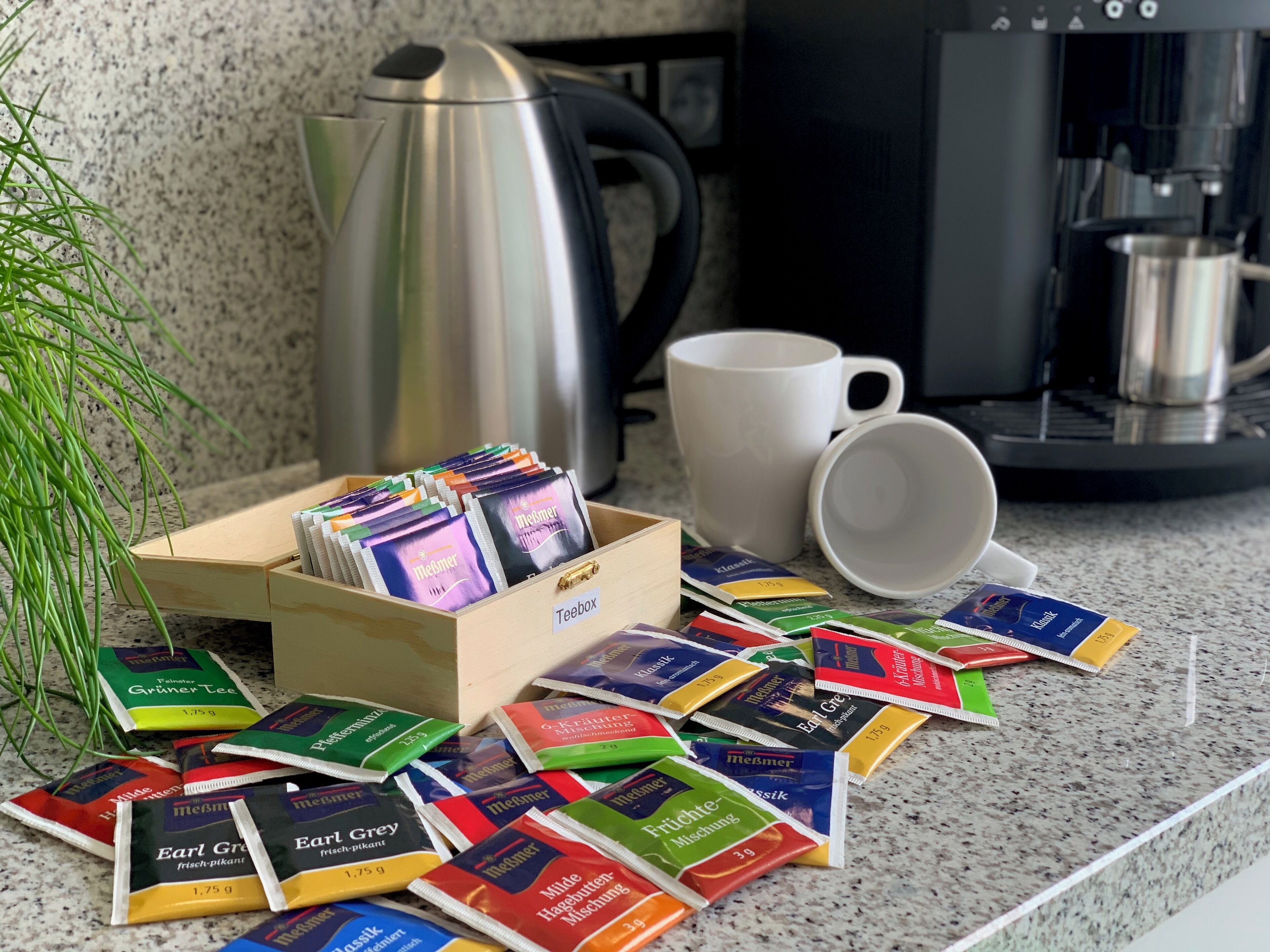 A kitchen counter with a teabox, coffee maker, and scattered tea packets.
