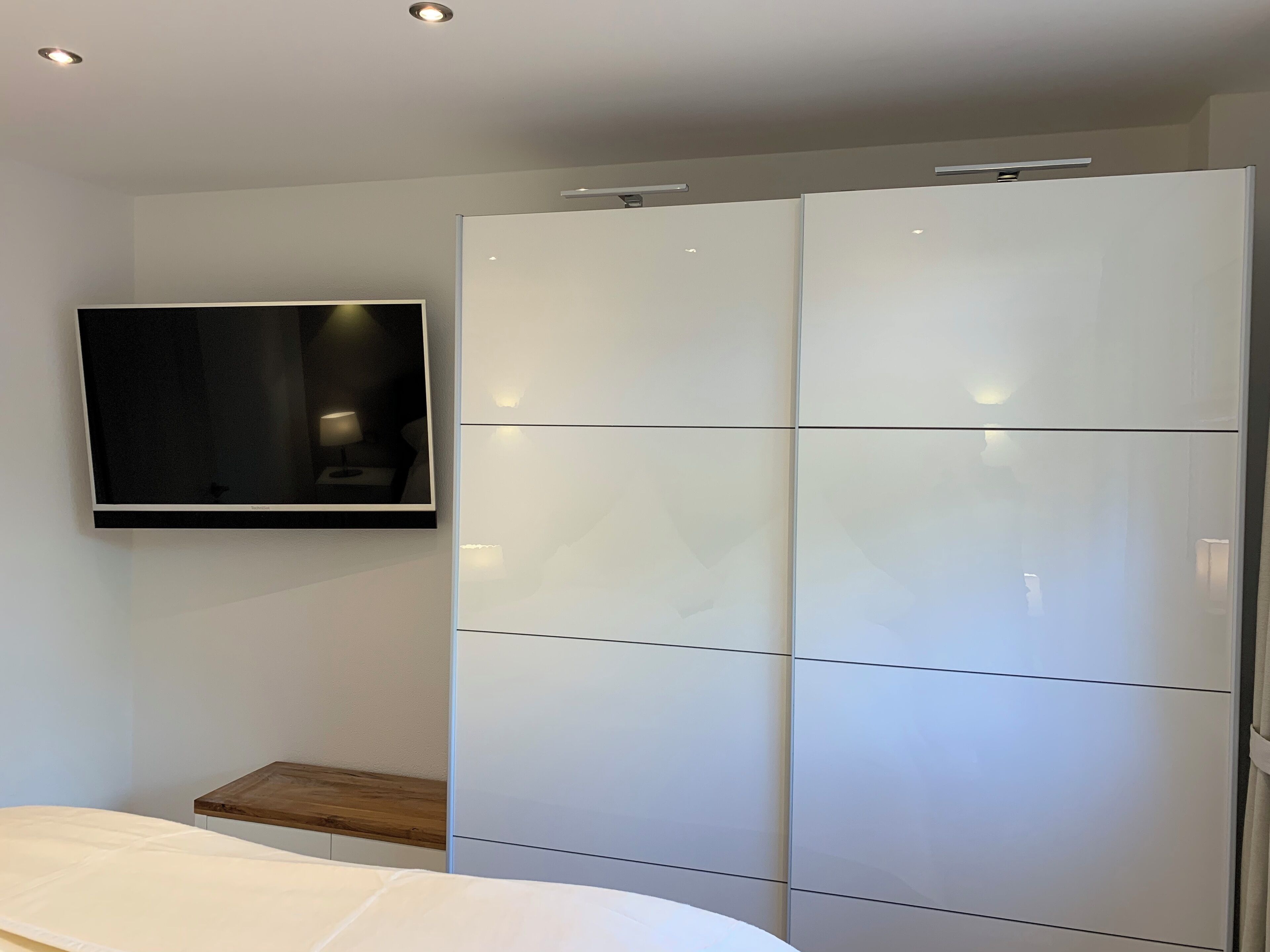 A bedroom with a bed, a TV mounted on the wall, and a wardrobe.