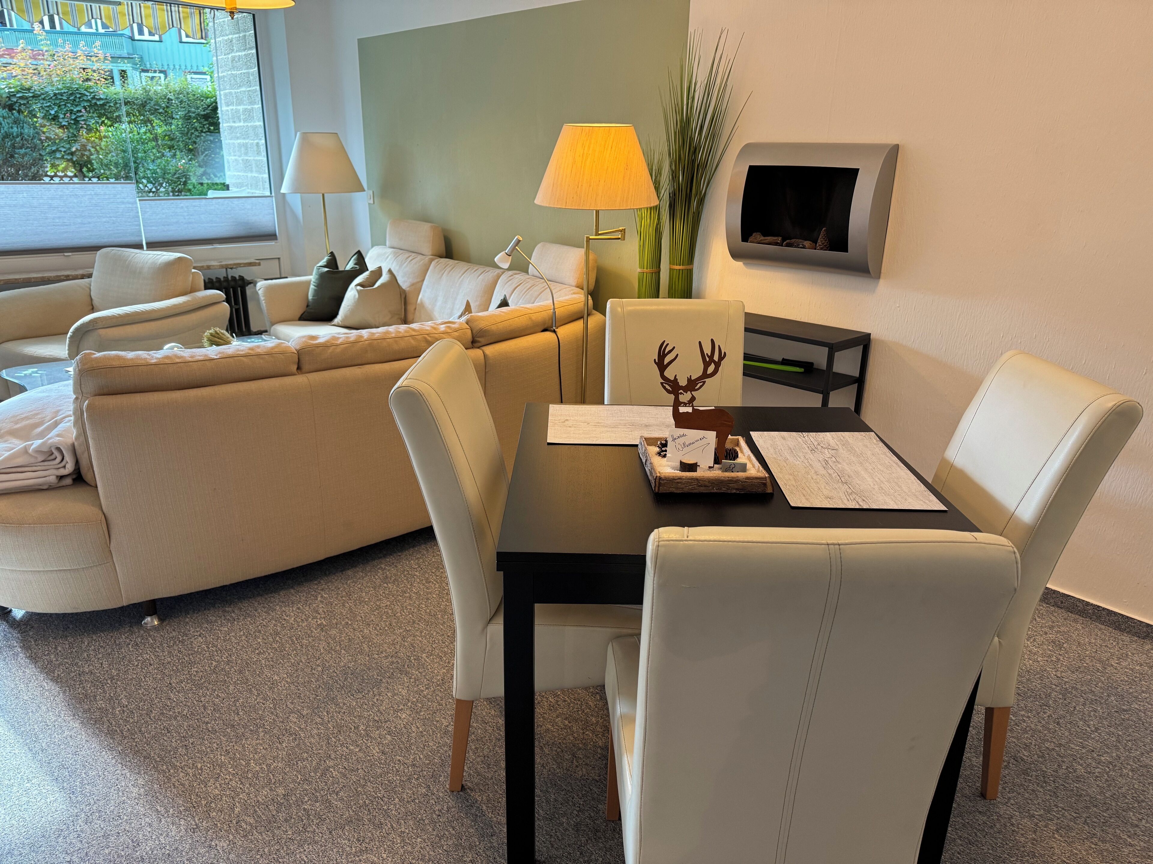 A modern hotel room with a sofa, a dining table with chairs, a lamp, and a fireplace.