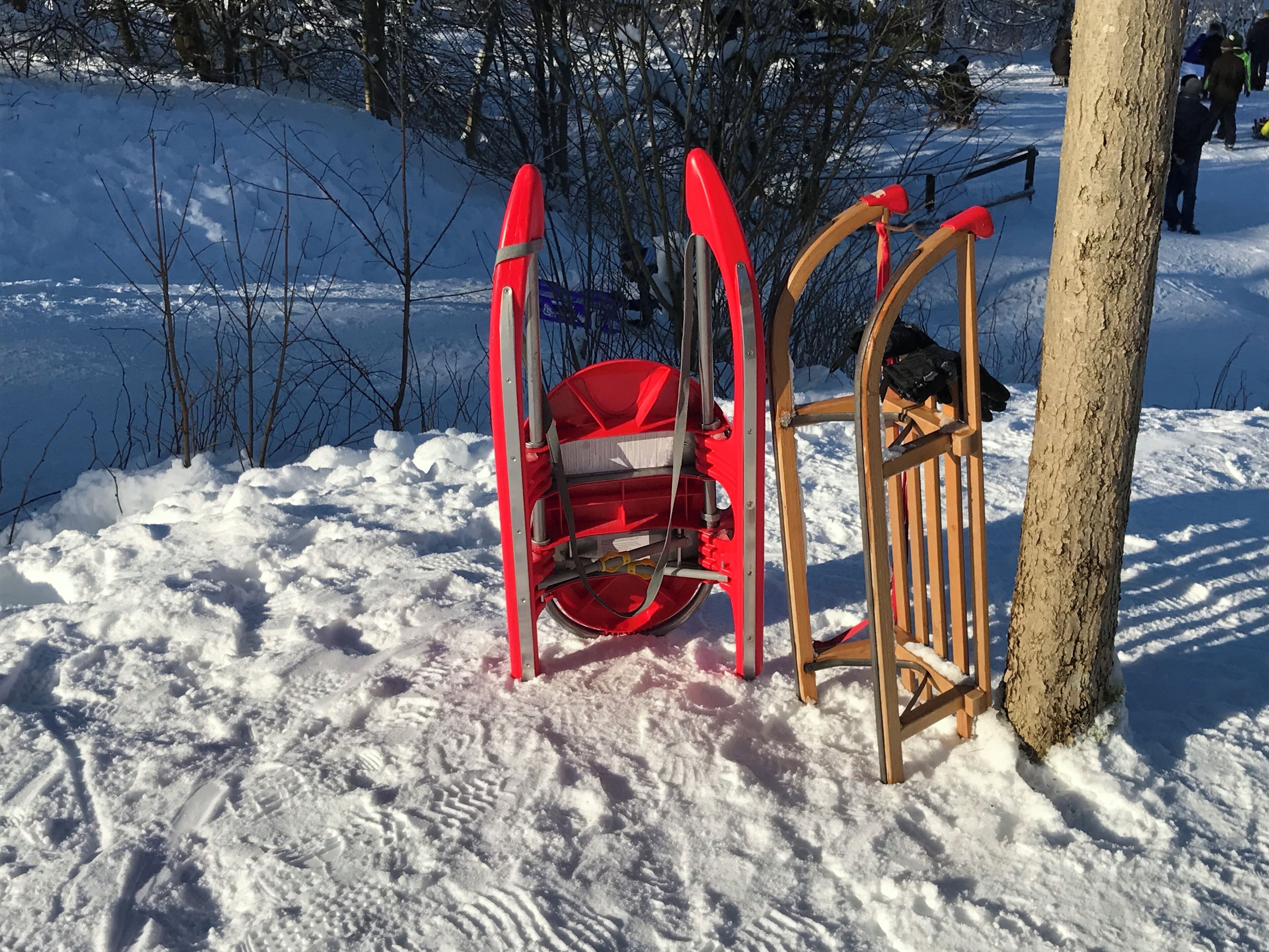 A red snow blower and a wooden chair in a snowy outdoor area.