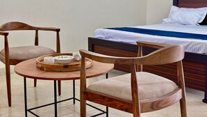 A bedroom with a bed, two wooden chairs, a small round table with a tray, and a white pillow.