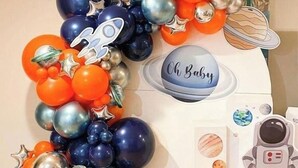 A space-themed decoration with balloons, a rocket cutout, and a baby name tag.