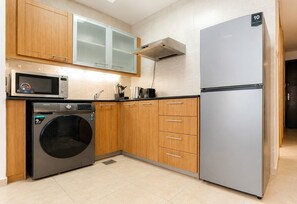 A compact kitchen with wooden cabinets, a stainless steel refrigerator, a microwave, and a built-in washing machine.