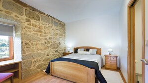 Ein Schlafzimmer mit Steinwand, Holzbett, Nachttischen und einem Schreibtisch mit Stuhl.
