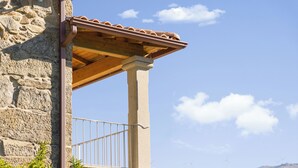 Ein Steinhaus mit einem Balkon, einer hölzernen Pergola und einer Aussicht auf Windkraftanlagen in der Ferne.