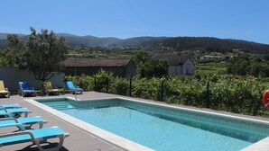 Ein rechteckiger Swimmingpool mit einer gefliesten Kante, umgeben von Liegestühlen und einem Baum.