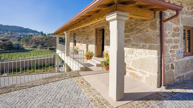 Ein Steinhaus mit überdachter Terrasse, einer Steintreppe und Blick auf einen Weinberg.