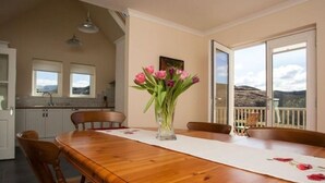 Un comedor con una mesa de madera, sillas, un florero y vistas al exterior a través de amplios ventanales.