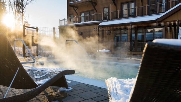 A pool area with lounge chairs and a steam feature, surrounded by buildings with balconies.