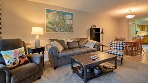 A living room with a gray sofa, a plaid armchair, a coffee table, and a map on the wall.