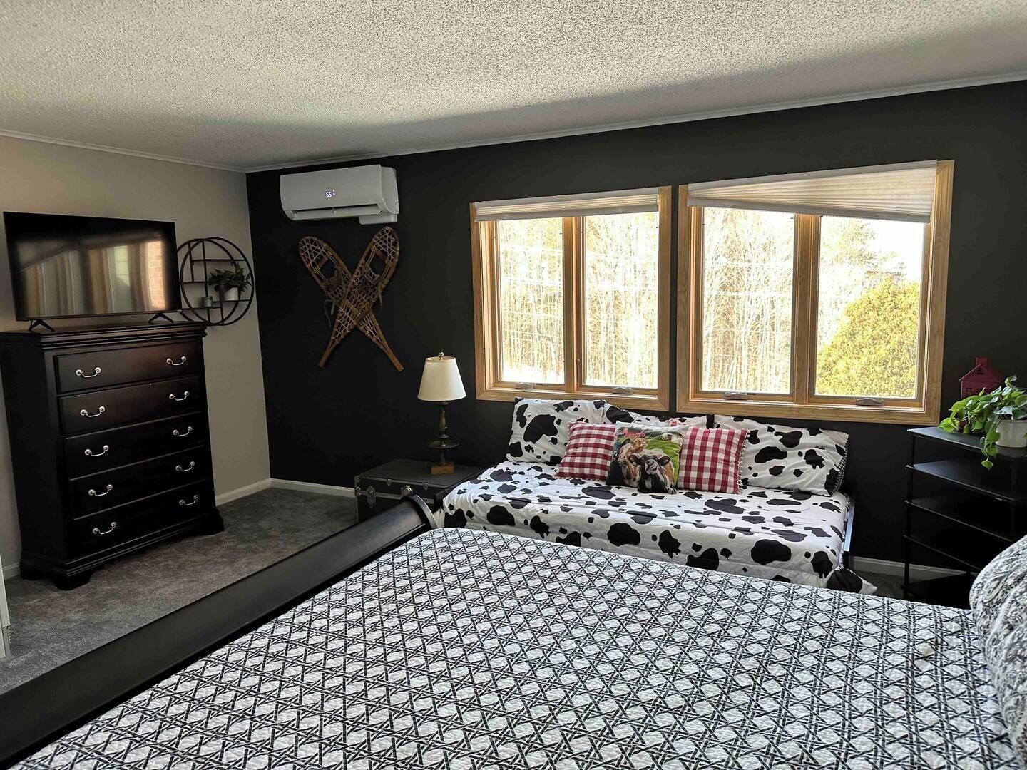 A bedroom with a bed, dresser, and a window with a view of trees.
