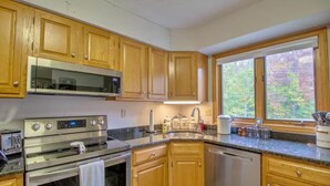 A kitchen with wooden cabinets, stainless steel appliances, a window with a view of trees, and a countertop with jars and utensils.