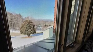 A room with a large window, a bed with a patterned cover, and a view of a building and trees outside.