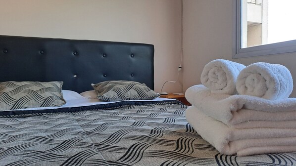 A neatly made bed with a patterned bedspread, two pillows, and rolled towels on the side. - Hornera Zeballos - Comfortable, accessible, HECA area (Rosario)