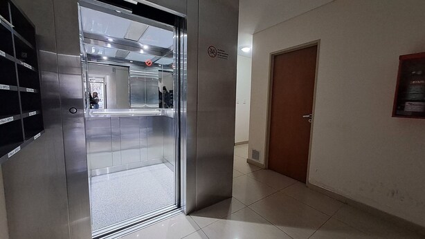 A hallway with a glass elevator door, a brown door, and a tiled floor.