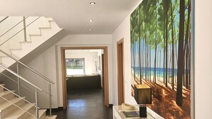 Et moderne interiør med en trappe, et skrivebord med lampe, og et stort maleri af et skovlandskab.
