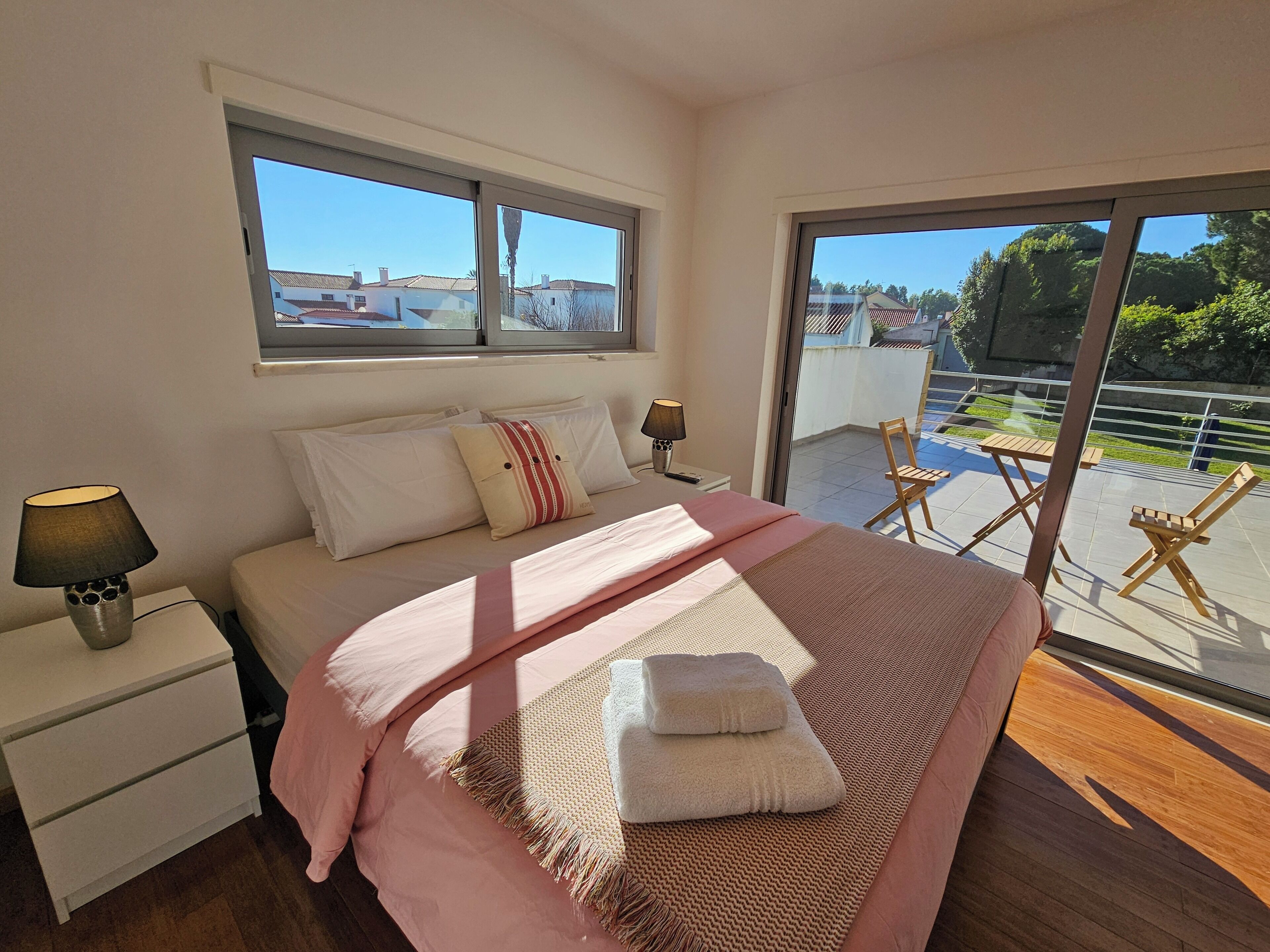 A bedroom with a bed, bedside tables, a window, and a balcony with chairs.