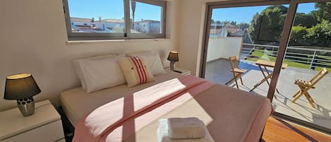 A bedroom with a bed, bedside tables, a window, and a balcony with chairs.