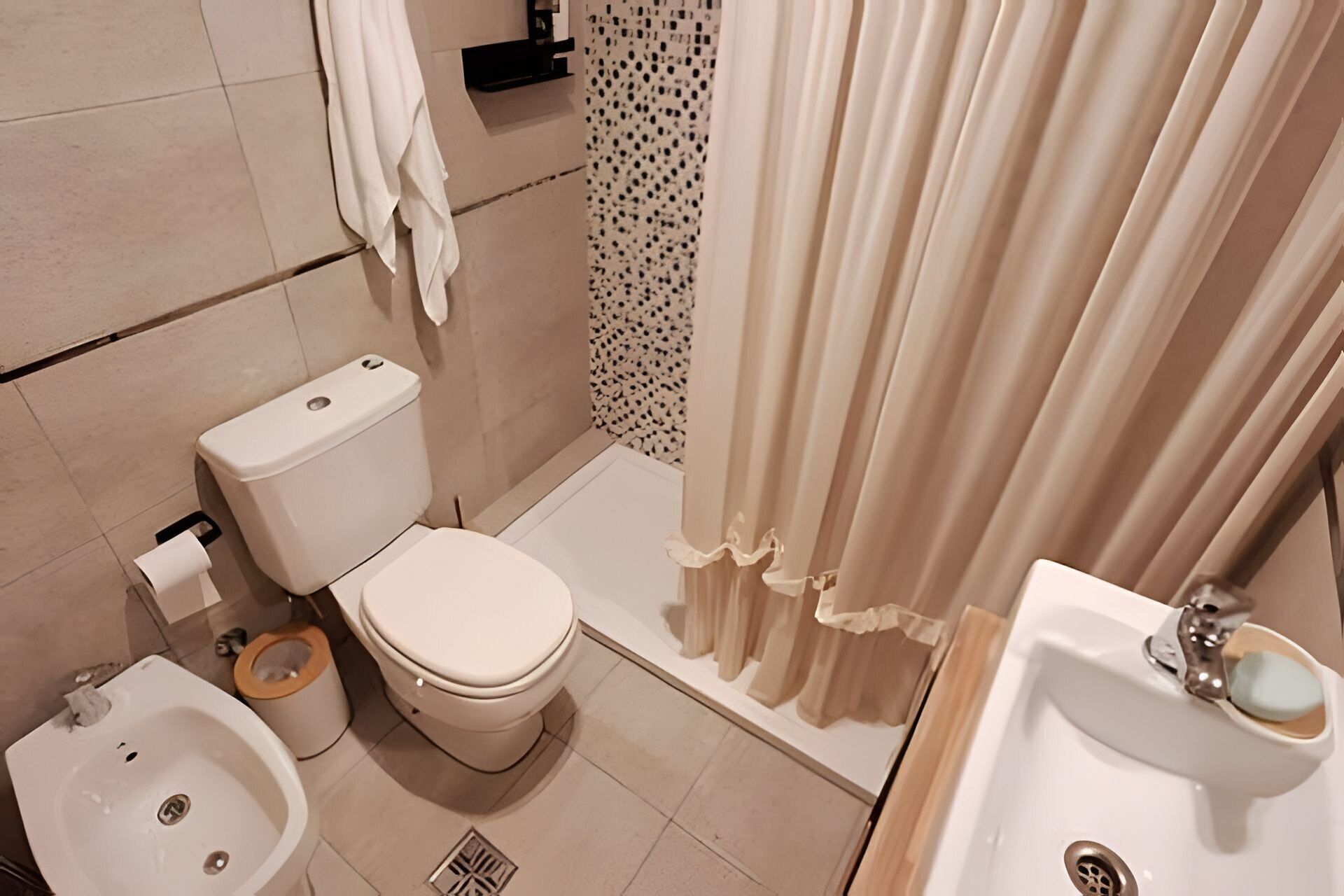 A bathroom with a toilet, bidet, sink, and shower curtain.