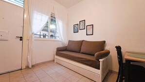 A small, cozy room with a brown sofa, a window with sheer curtains, a door, and three framed pictures on the wall. - Dorados Güemes - Fully accessible at Pichincha (Rosario)