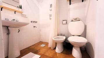 A small bathroom with a sink, two toilets, a shower curtain, and a toilet paper holder.