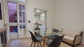 Un'area pranzo moderna con un tavolo in vetro e sedie nere, un divano beige e una cucina sullo sfondo.