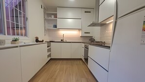 Una cucina moderna con mobili bianchi, pavimento in legno e una finestra con sbarre.