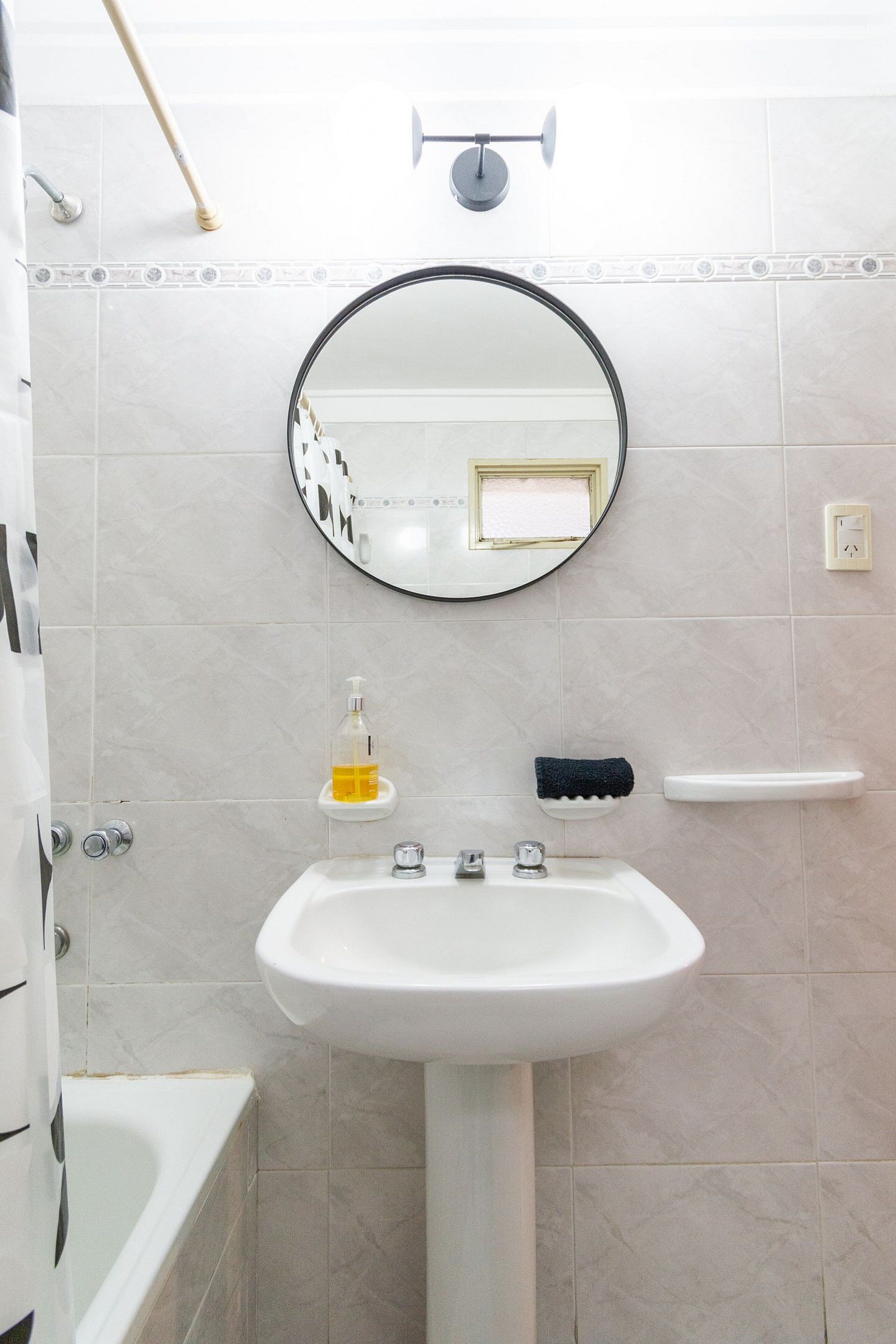 Un bany amb un lavabo blanc, un mirall, un dispensador de sabó i una barra de tovalloles.