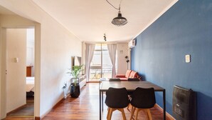 A modern living room with a wooden floor, a dining table with chairs, a blue accent wall, and a ceiling light fixture. - Hornera Coti - Modern, comfortable, ideal location. (Rosario)