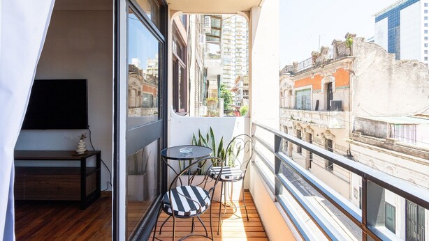 A balcony with a wooden floor, a small table, two chairs, and a TV. - Hornera Coti - Modern, comfortable, ideal location. (Rosario)