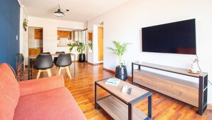 A modern living room with a sofa, coffee table, and TV. There is a dining area with chairs and a table in the background. - Hornera Coti - Modern, comfortable, ideal location. (Rosario)