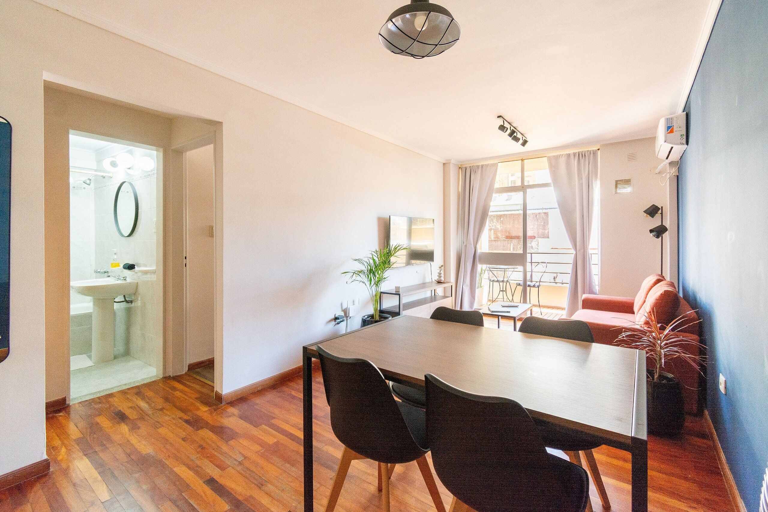 A modern living room with a wooden dining table, black chairs, a sofa, and a potted plant.