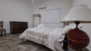 Une chambre à coucher comprenant un lit, une commode, une chaise, une lampe et un appareil de climatisation.