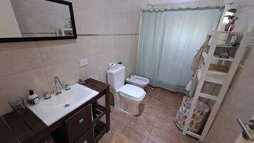 Een badkamer met een wastafel, toilet, bidet en een plank met toiletartikelen.