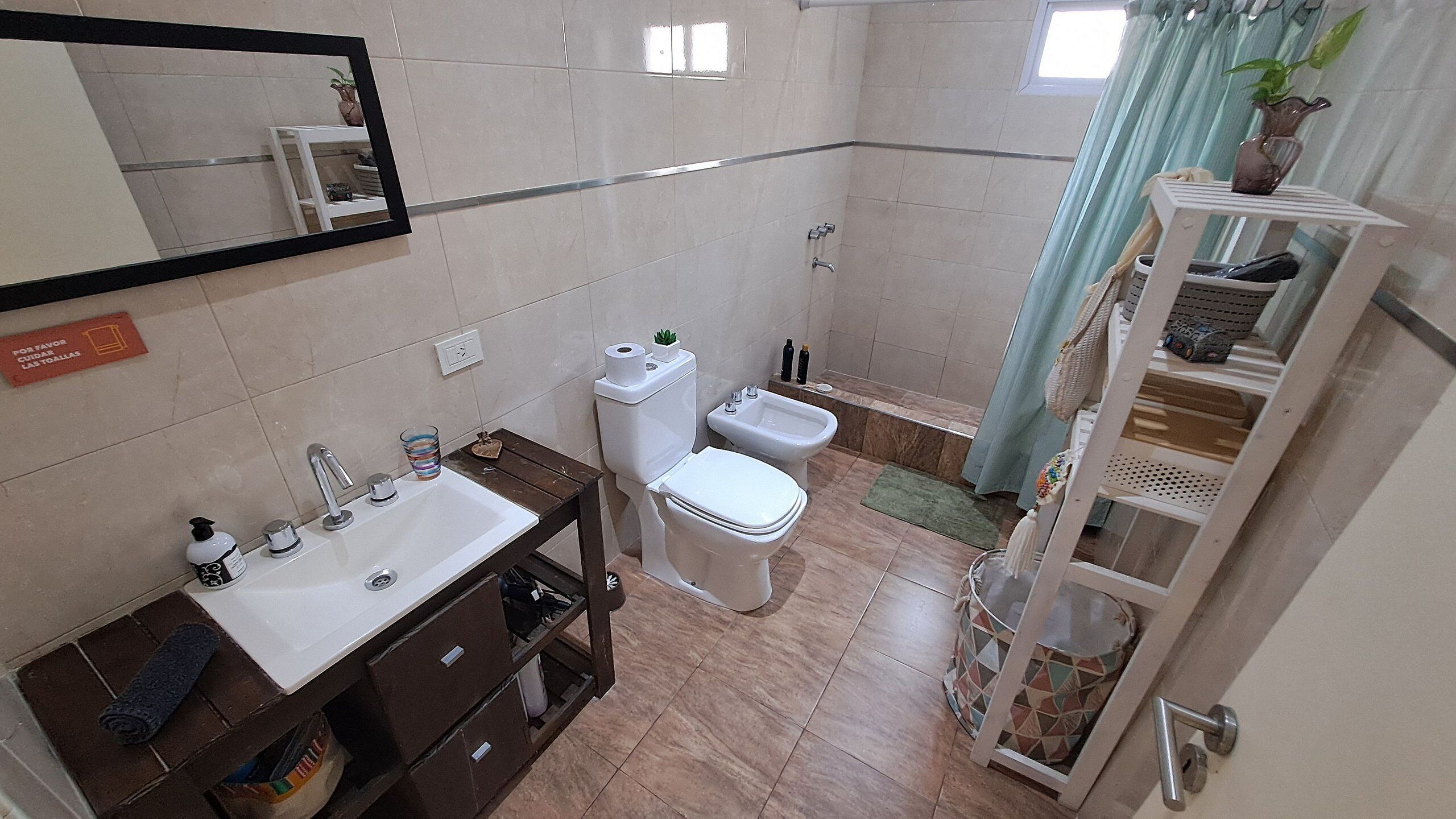 A bathroom with a white sink, toilet, and bidet, a mirror, and a shelf with toiletries.