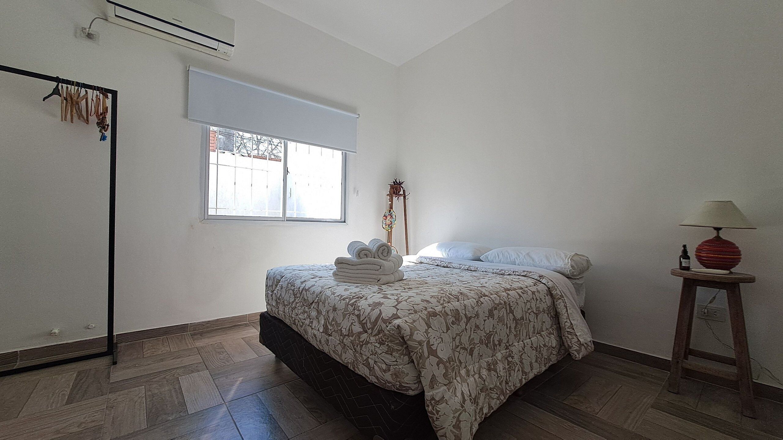 Un dormitorio con cama, ventana, lámpara de pie y perchero.