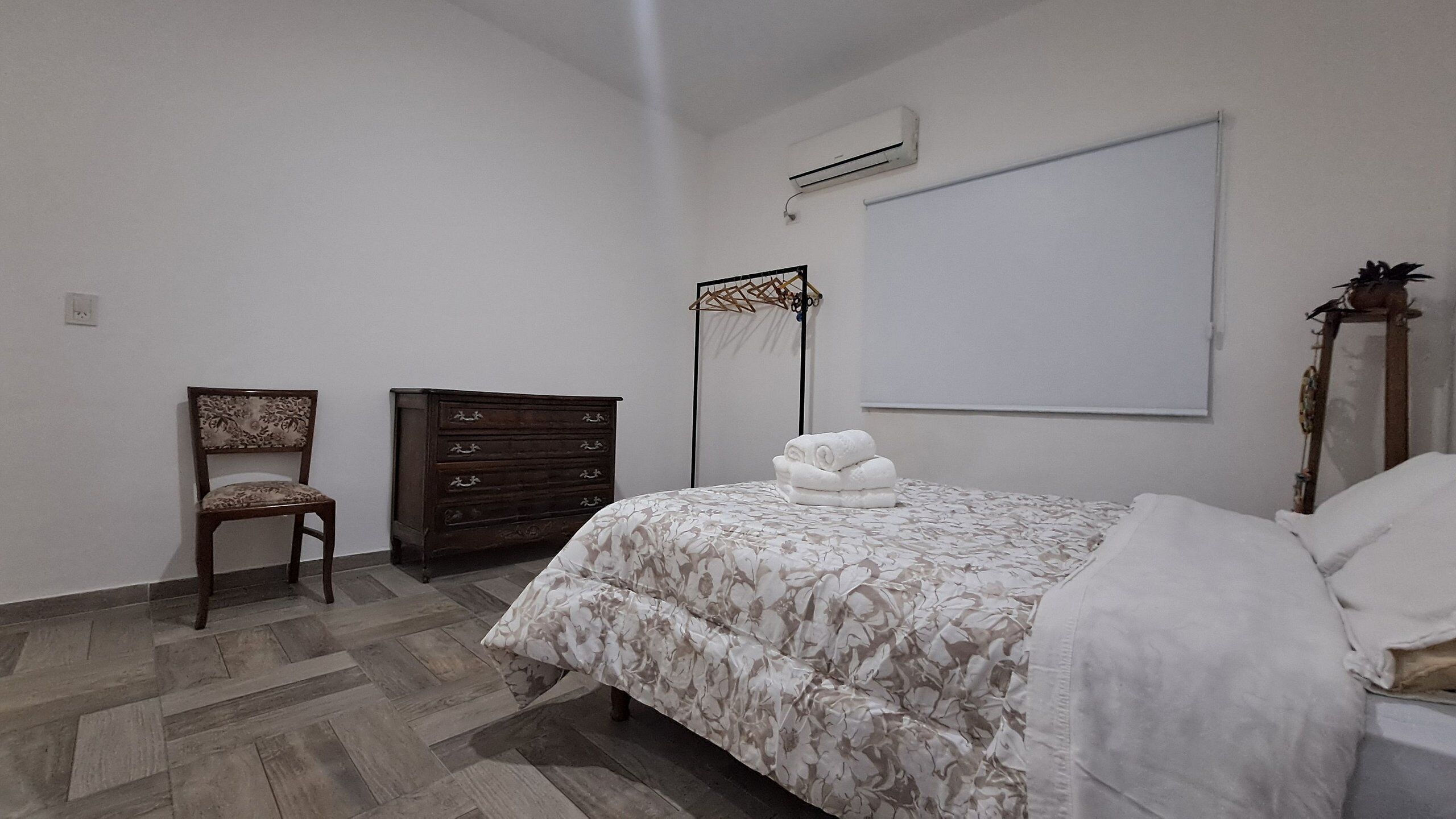 A bedroom with a bed, a wooden dresser, a chair, and a wall-mounted air conditioning unit.