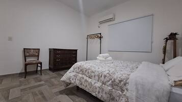 A bedroom with a bed, a wooden dresser, a chair, and a wall-mounted air conditioning unit.