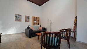 Un salon avec un canapé noir, deux fauteuils en bois, une table basse et une bibliothèque.